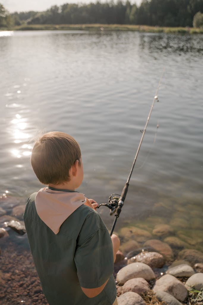 Boy scout fishing with a rod by a serene lake, enjoying peaceful leisure outdoors.